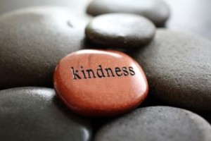 The word Kindness carved in goldstone resting on river rocks.